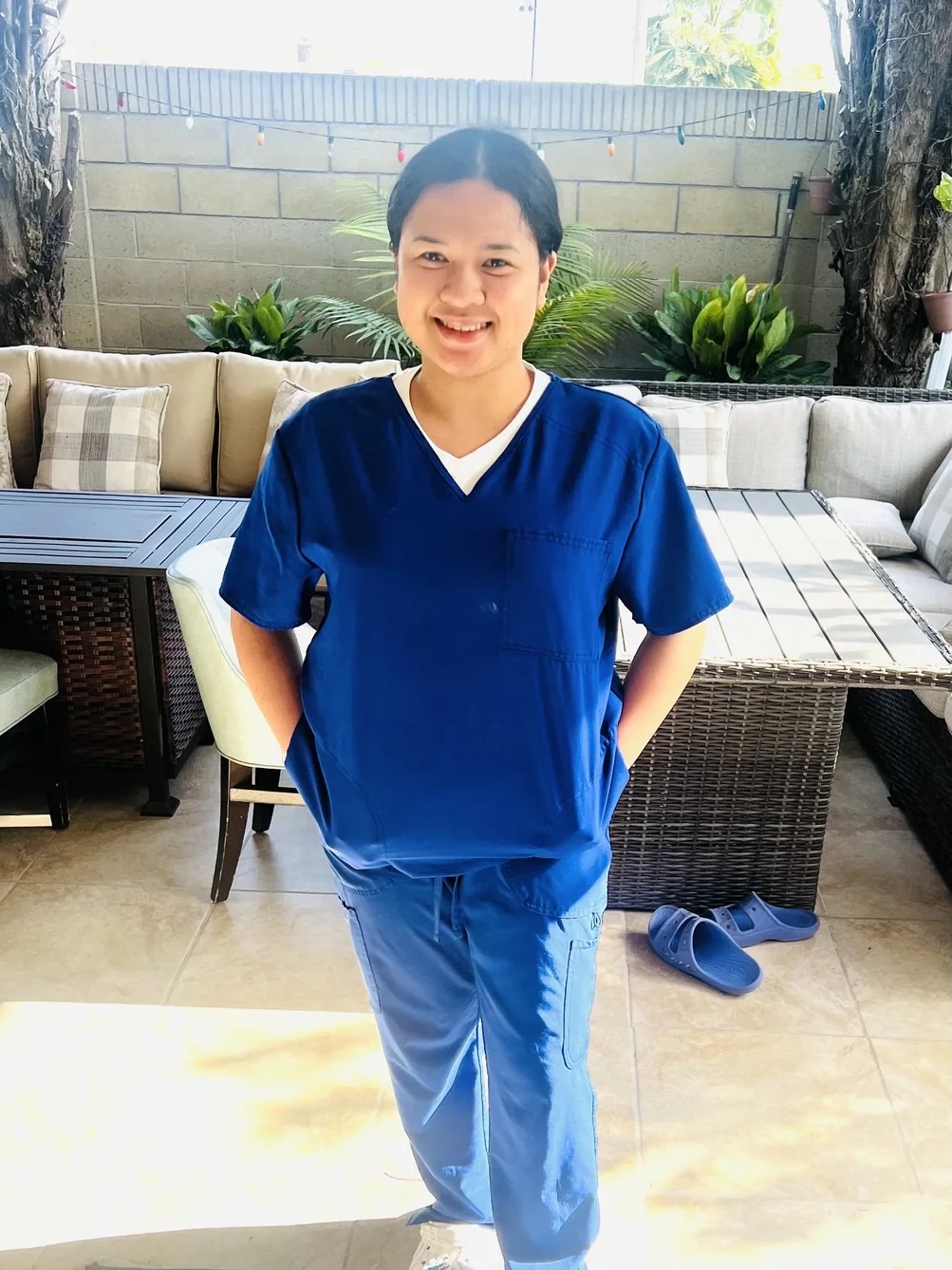 Smiling caregiver in blue medical scrubs standing in outdoor patio area