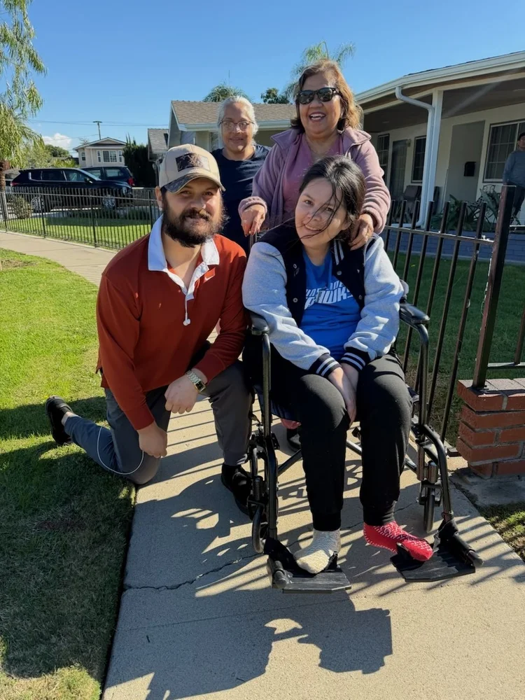 Resident in wheelchair with three caregivers smiling together outside the care home