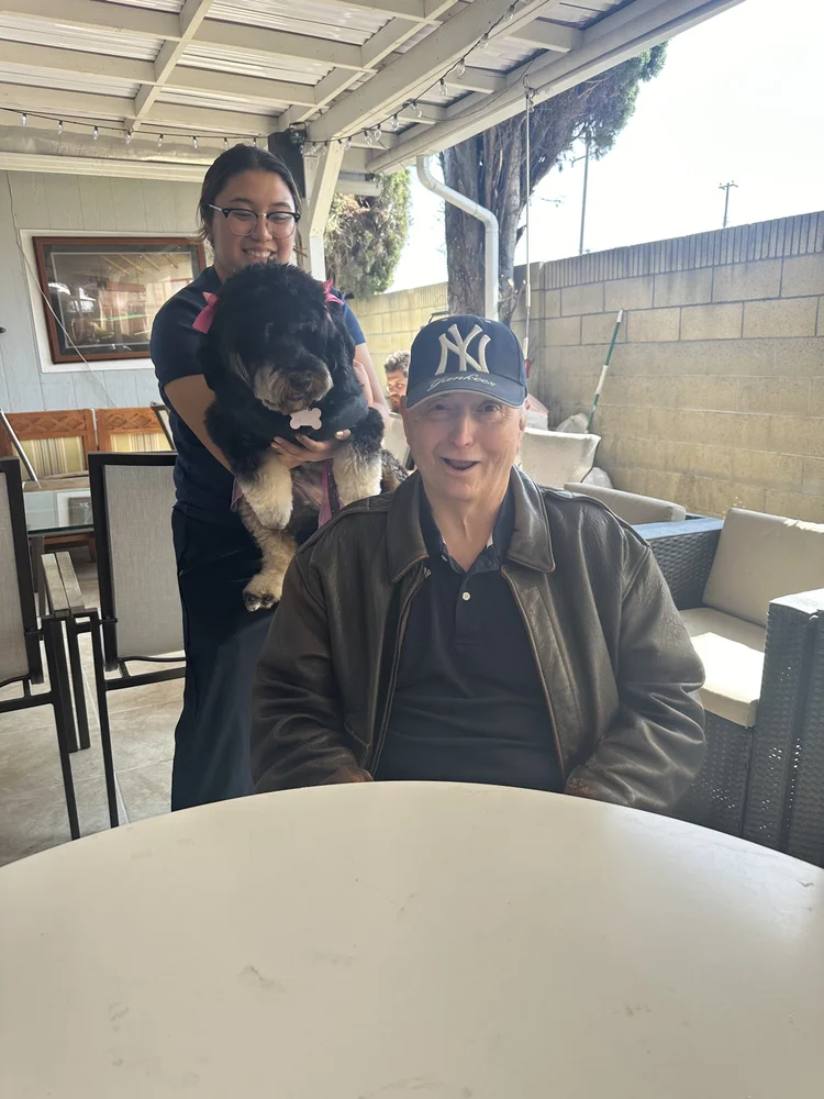 Resident with visitor and therapy dog enjoying time together on outdoor patio